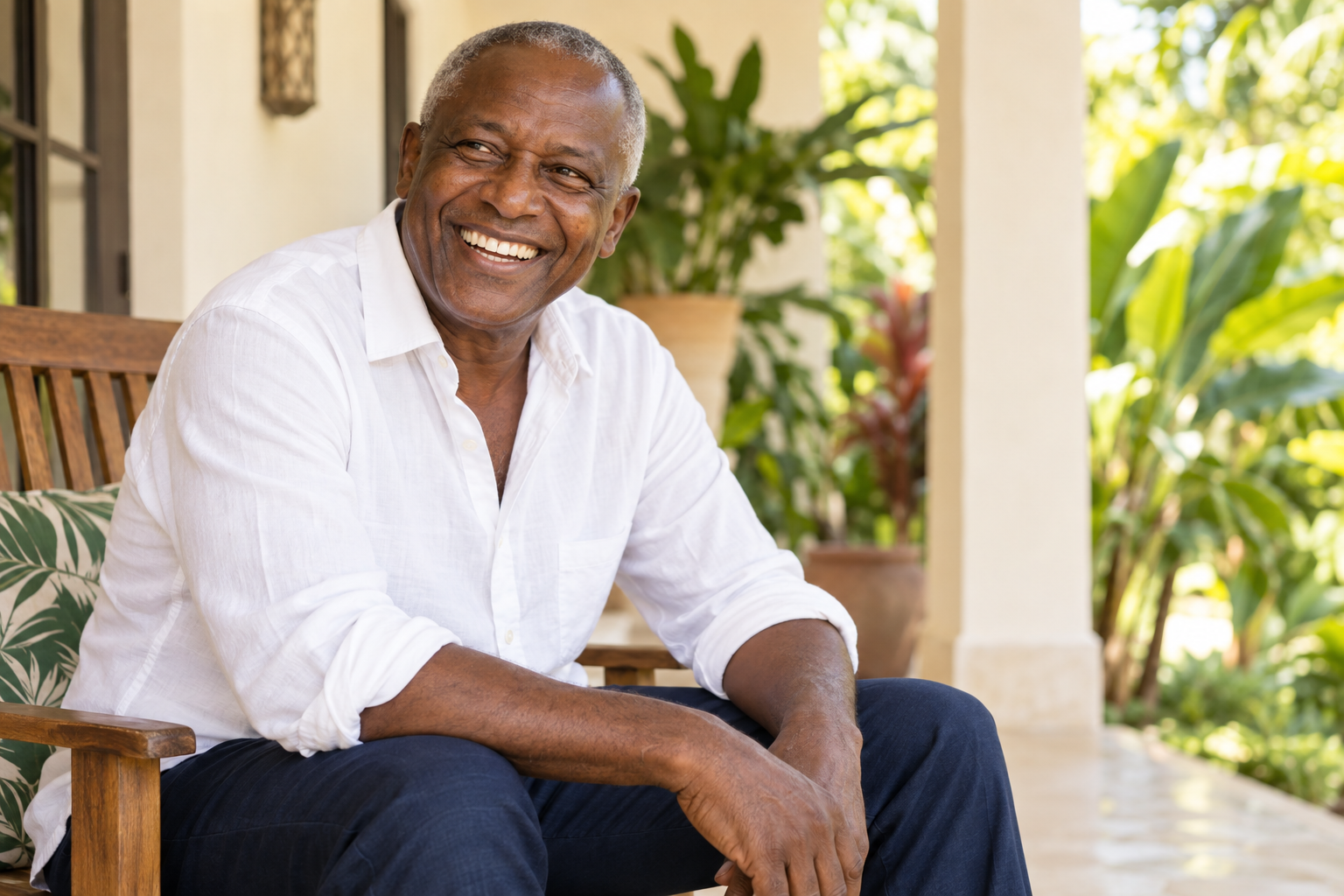 A smiling older African man in a white shirt seated on a veranda